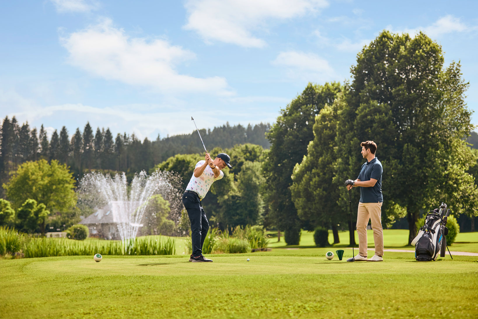 Zwei Golfer auf einem grünen Golfplatz mit Teich