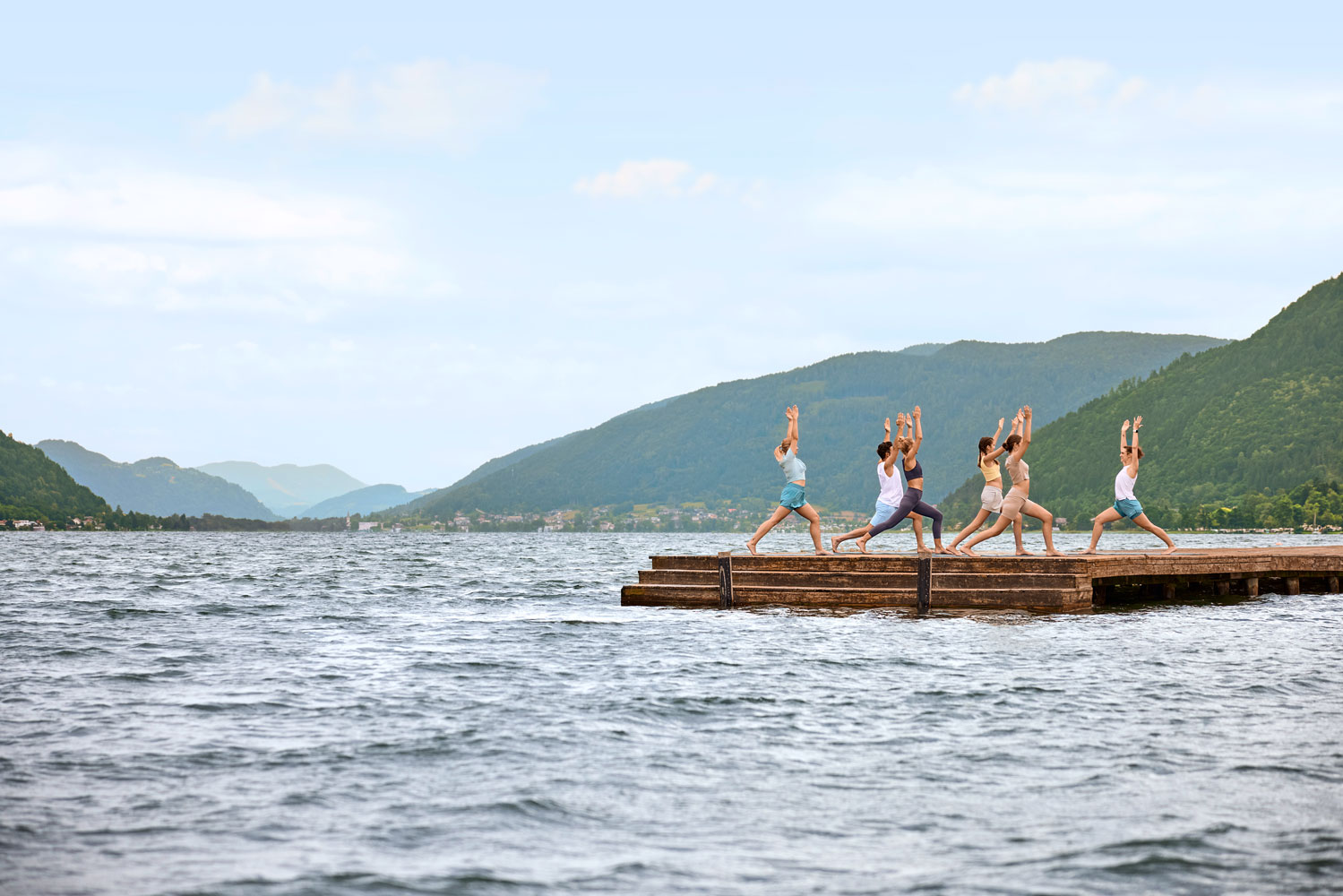 Vier Personen üben Yoga auf einer schwimmenden Plattform am See