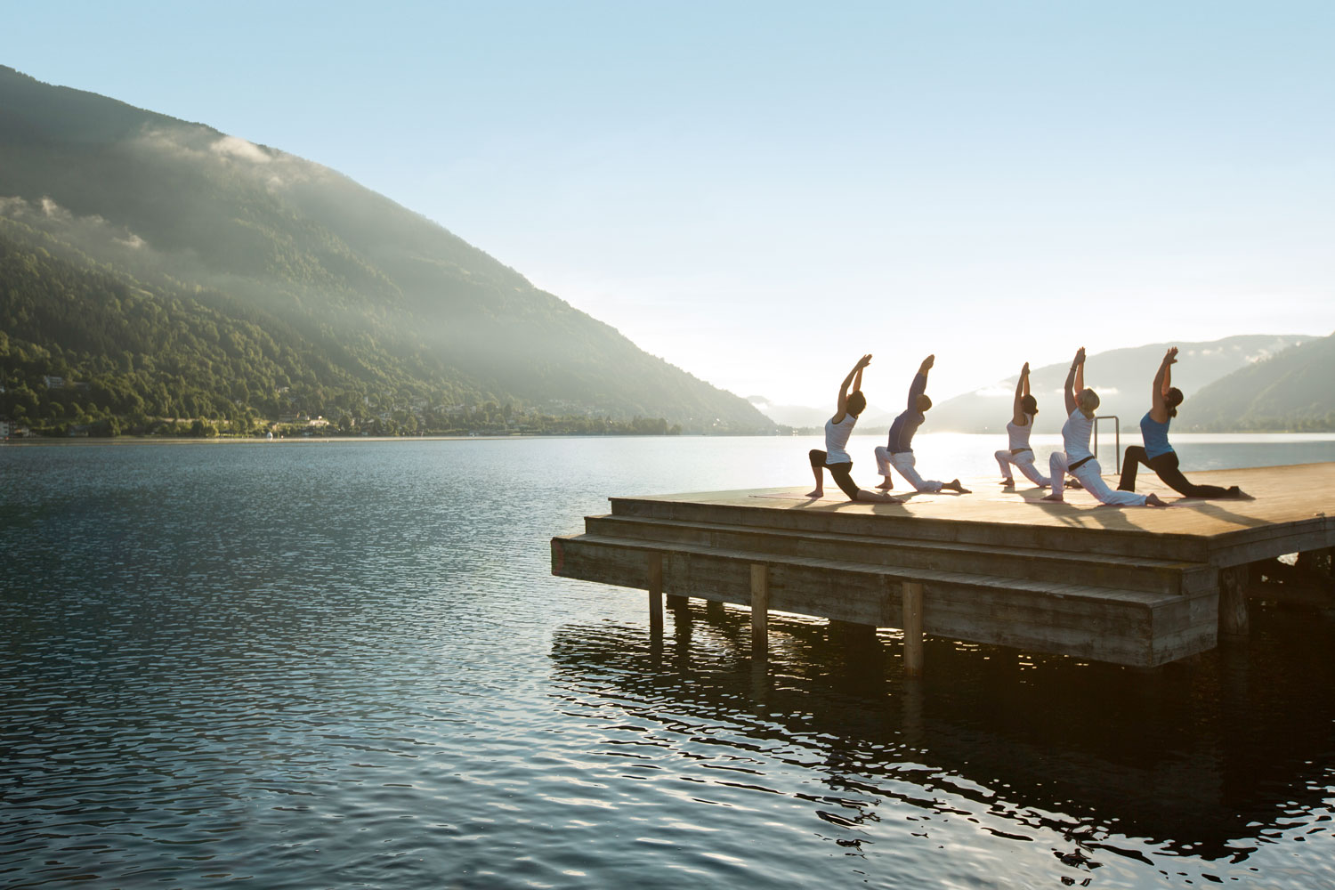 Yogagruppe auf einem Steg im Sonnenlicht vor der Bergkulisse